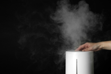 Photo of Woman using modern air humidifier on black background, closeup. Space for text