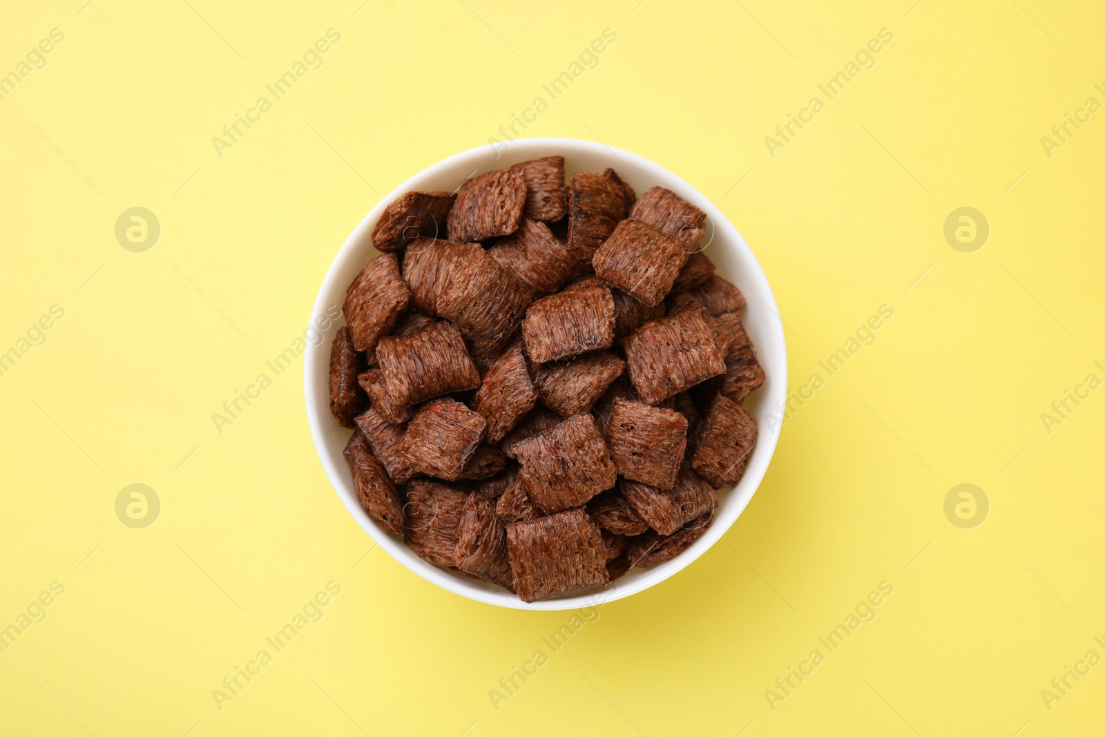 Photo of Chocolate cereal pads in bowl on yellow table, top view