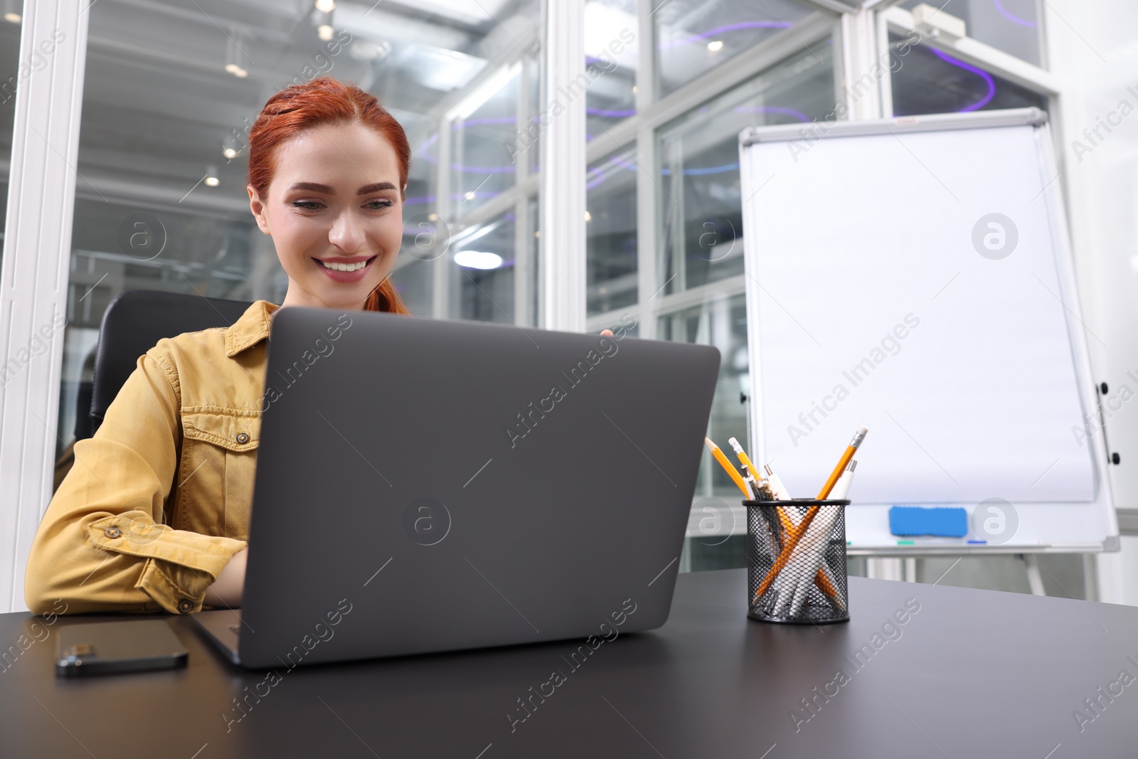 Photo of Happy woman working with laptop at black desk in office