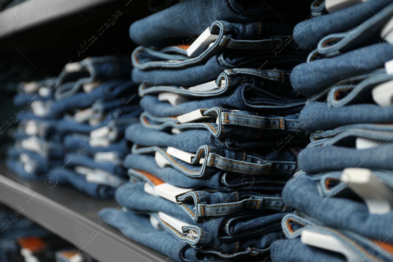 Photo of Collection of modern jeans on shelf in shop, closeup