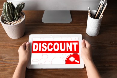 Woman holding tablet with word Discount at table, closeup