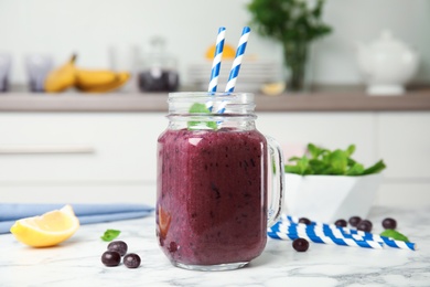 Photo of Mason jar with delicious acai smoothie on table in kitchen