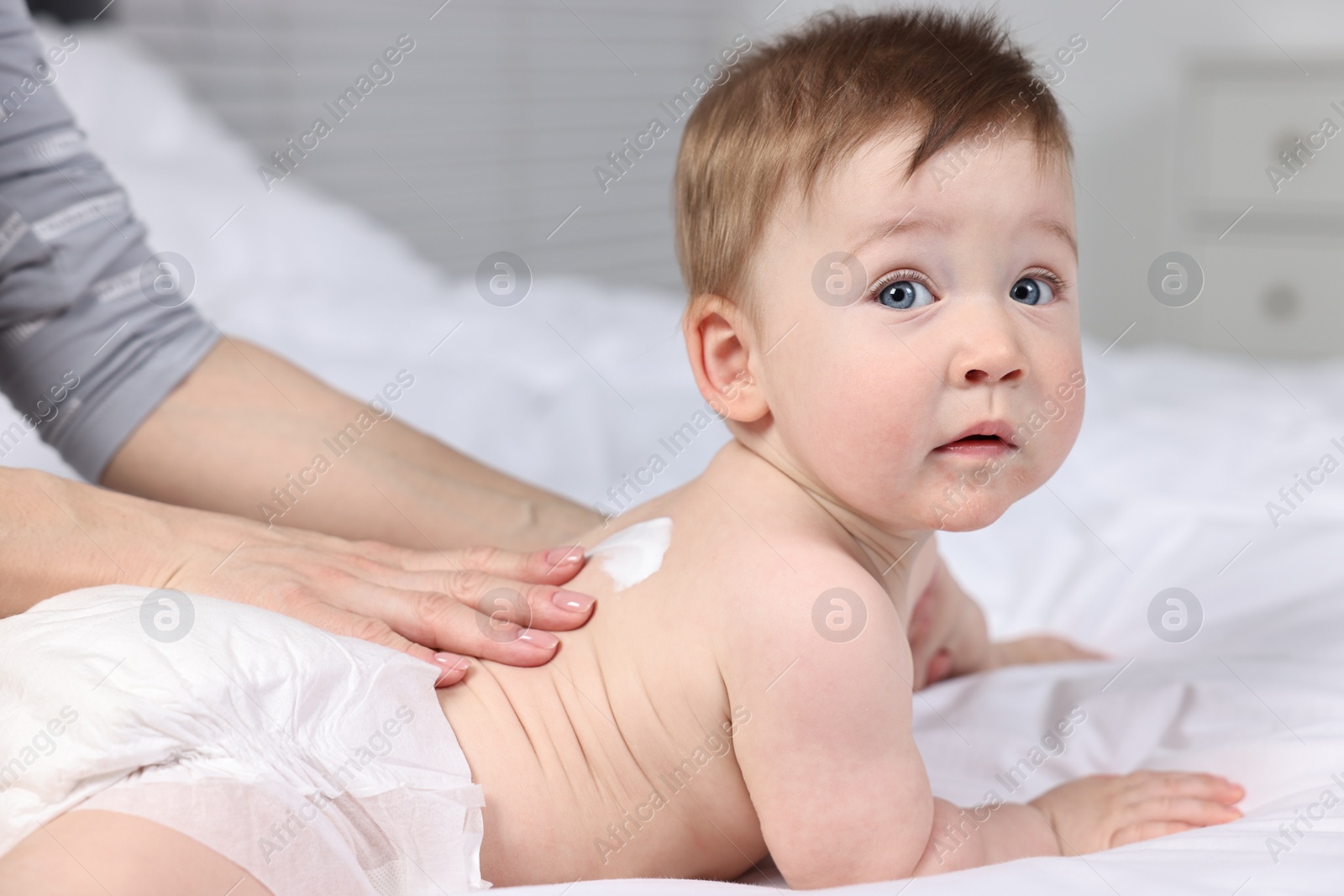 Photo of Woman applying body cream onto baby`s back on bed, closeup