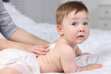 Woman applying body cream onto baby`s back on bed, closeup