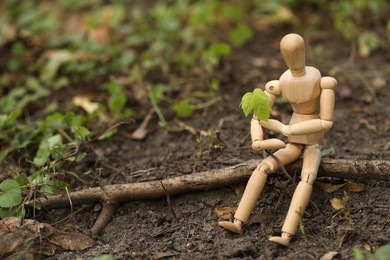 Photo of Wooden human figure with young green seedling on soil outdoors, space for text