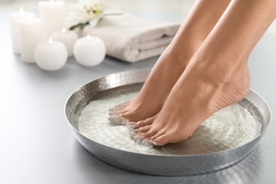 Photo of Closeup view of woman soaking her feet in dish with water on grey floor. Spa treatment