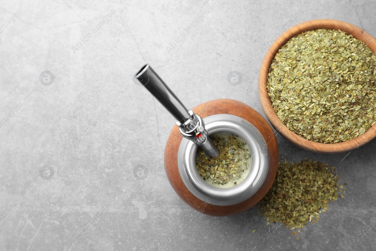 Photo of Calabash with bombilla and bowl of mate tea leaves on grey table, flat lay. Space for text