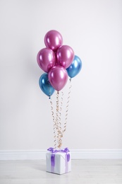 Photo of Bright balloons and gift box on floor against white wall