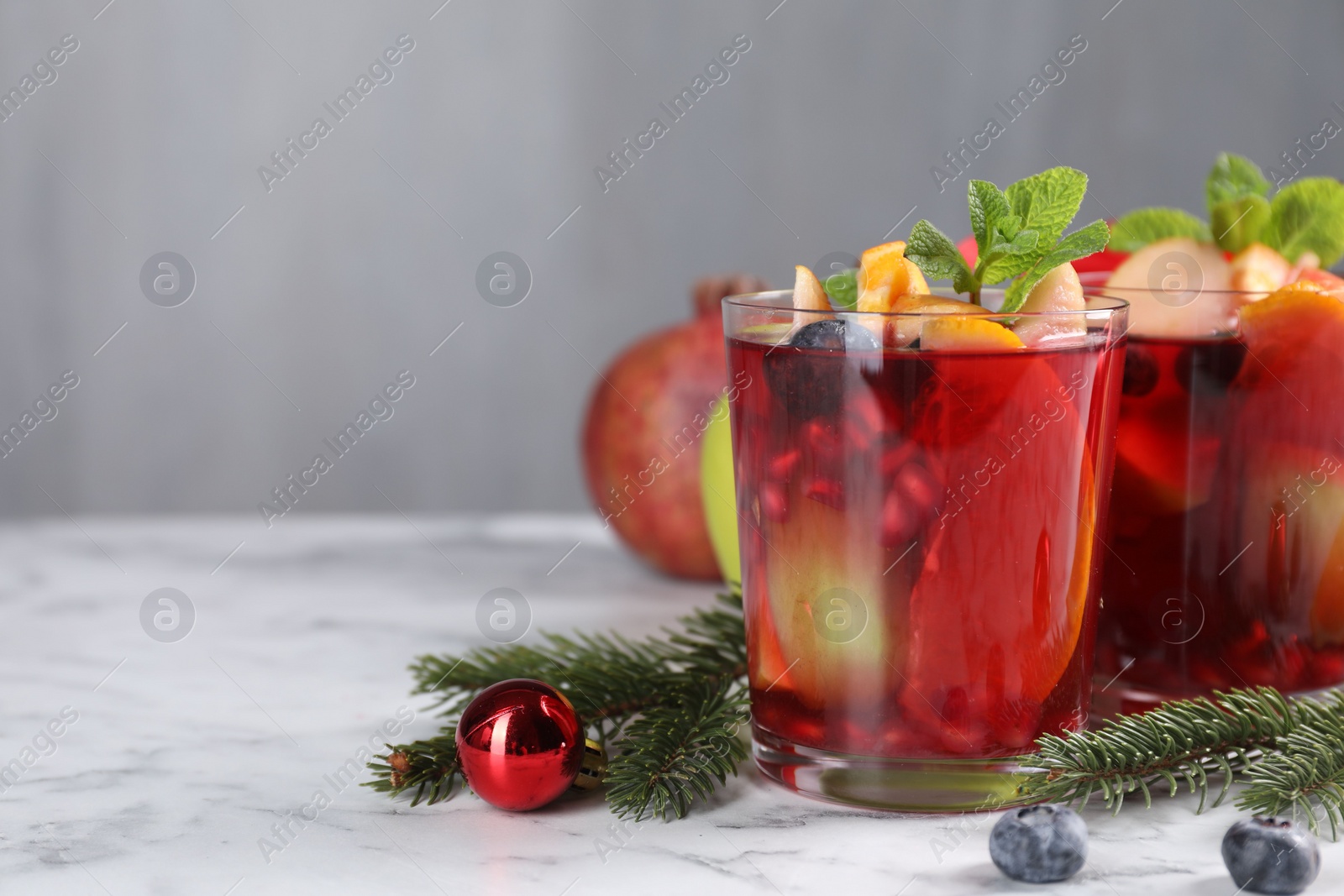 Photo of Aromatic Sangria drink in glasses, ingredients and Christmas decor on white marble table, space for text