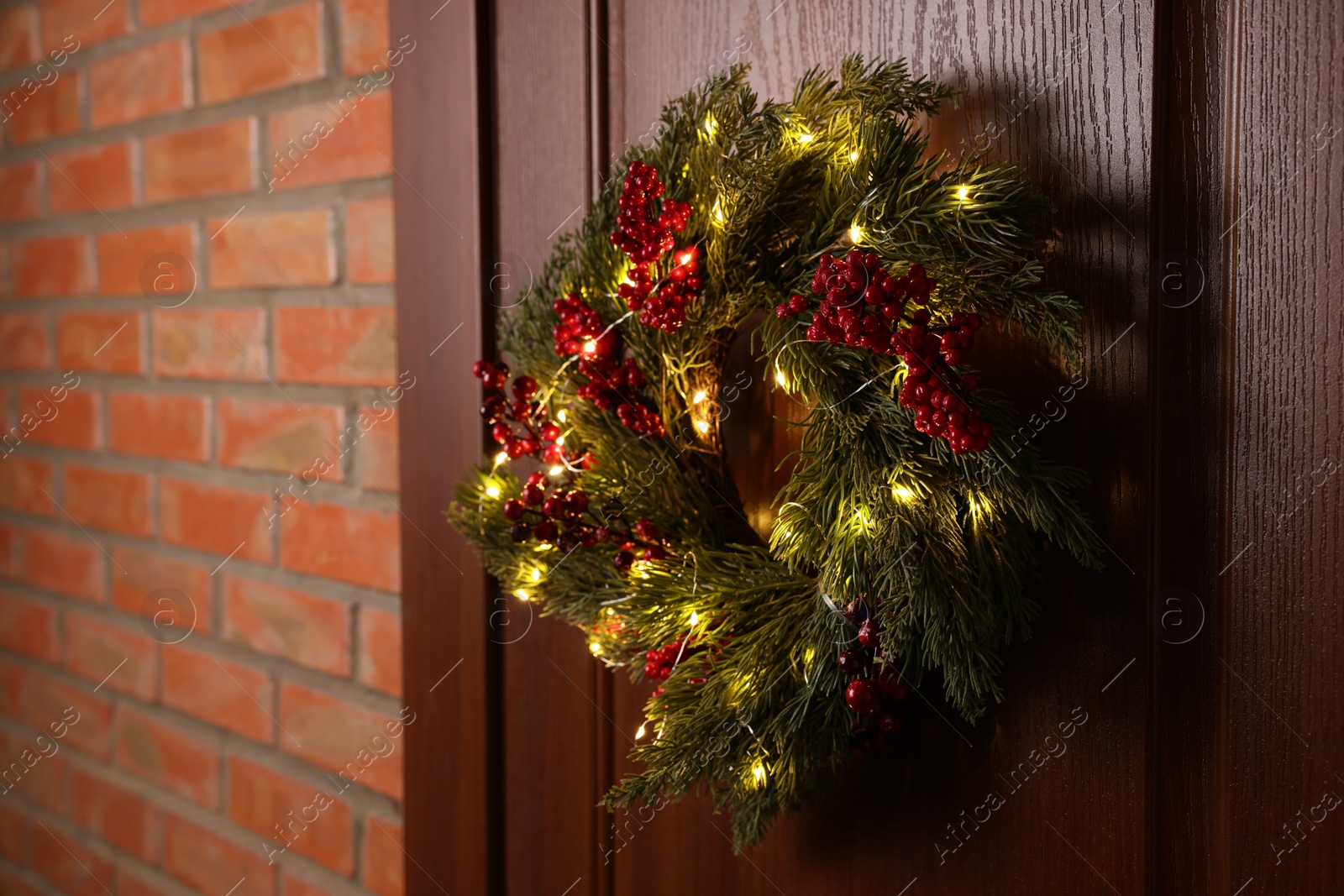 Photo of Beautiful Christmas wreath with red berries and fairy lights hanging on wooden door, space for text