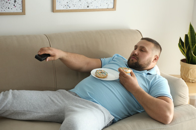 Lazy overweight man with donuts watching TV on sofa at home