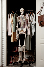 Photo of Artificial human skeleton model among clothes in wardrobe room
