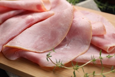Photo of Slices of delicious ham with thyme on wooden board, closeup