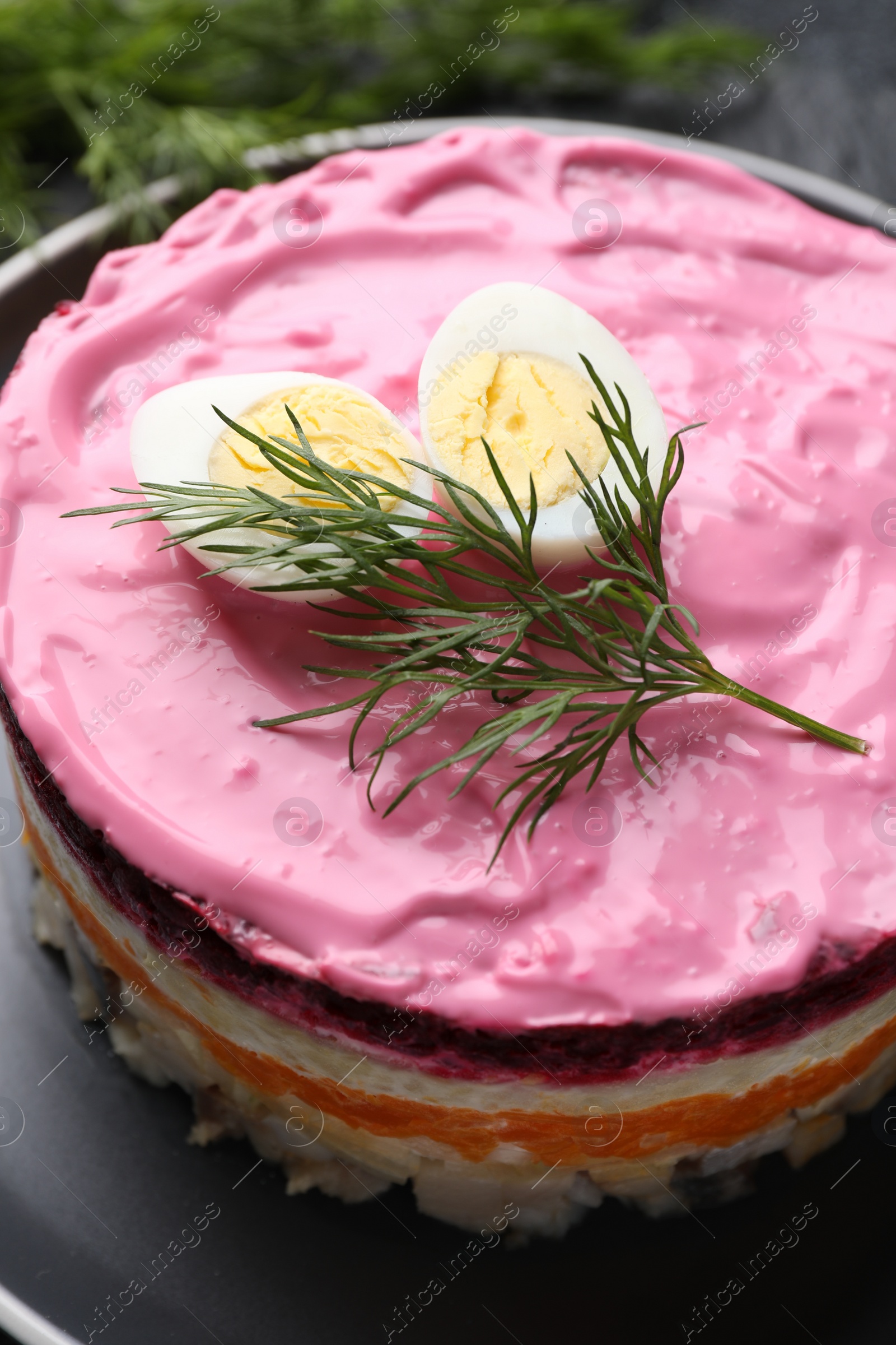 Photo of Herring under fur coat salad on black plate, closeup. Traditional Russian dish