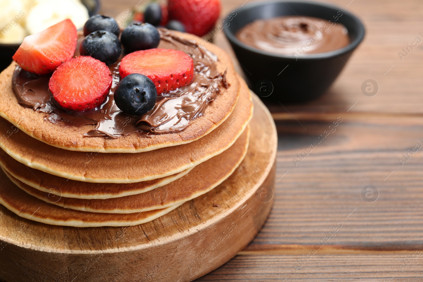 Photo of Tasty pancakes with chocolate paste and berries on wooden table, closeup. Space for text