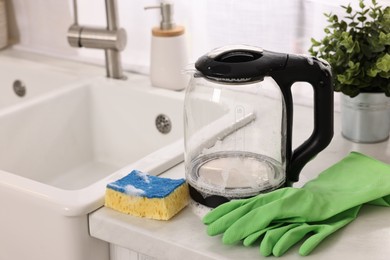 Cleaning electric kettle. Rubber gloves and sponge with foam on countertop in kitchen