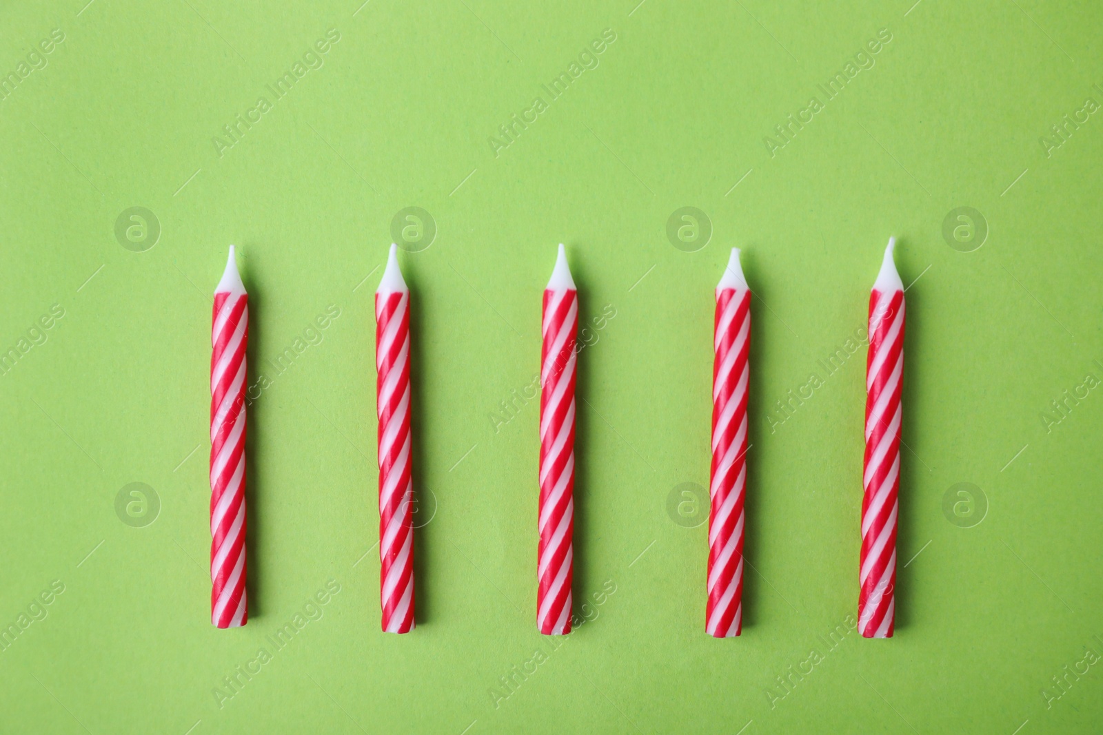 Photo of Red striped birthday candles on green background, top view