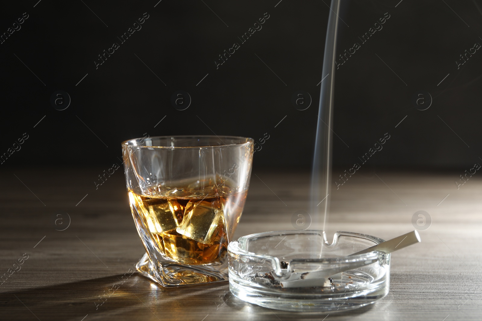 Photo of Alcohol addiction. Whiskey in glass, cigarettes and ashtray on wooden table