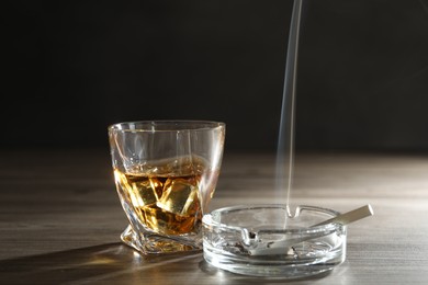 Photo of Alcohol addiction. Whiskey in glass, cigarettes and ashtray on wooden table