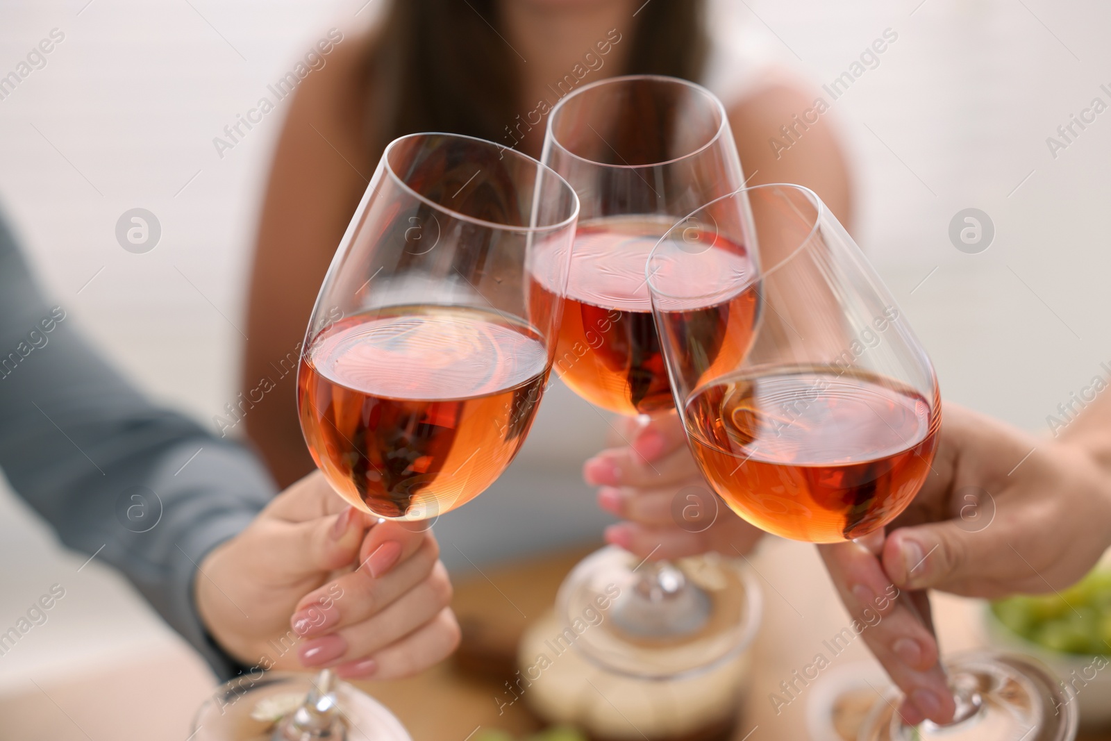 Photo of People clinking glasses with rose wine indoors, closeup