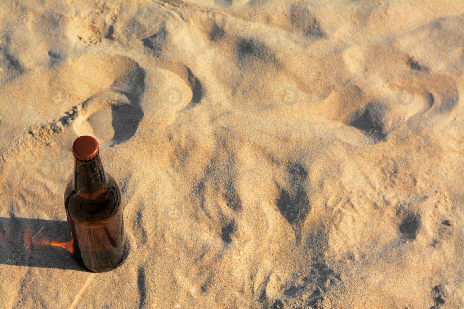 Photo of Bottle of beer on sandy beach, above view. Space for text