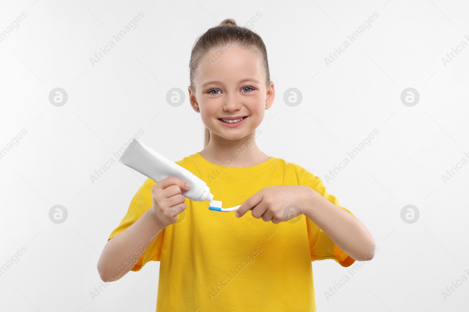 Photo of Happy girl squeezing toothpaste from tube onto toothbrush on white background