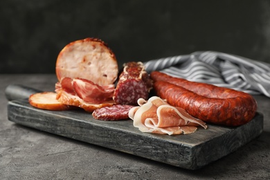 Photo of Cutting board with different meat delicacies on gray table