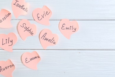 Photo of Choosing baby's name. Paper stickers with different names on white wooden background, flat lay. Space for text