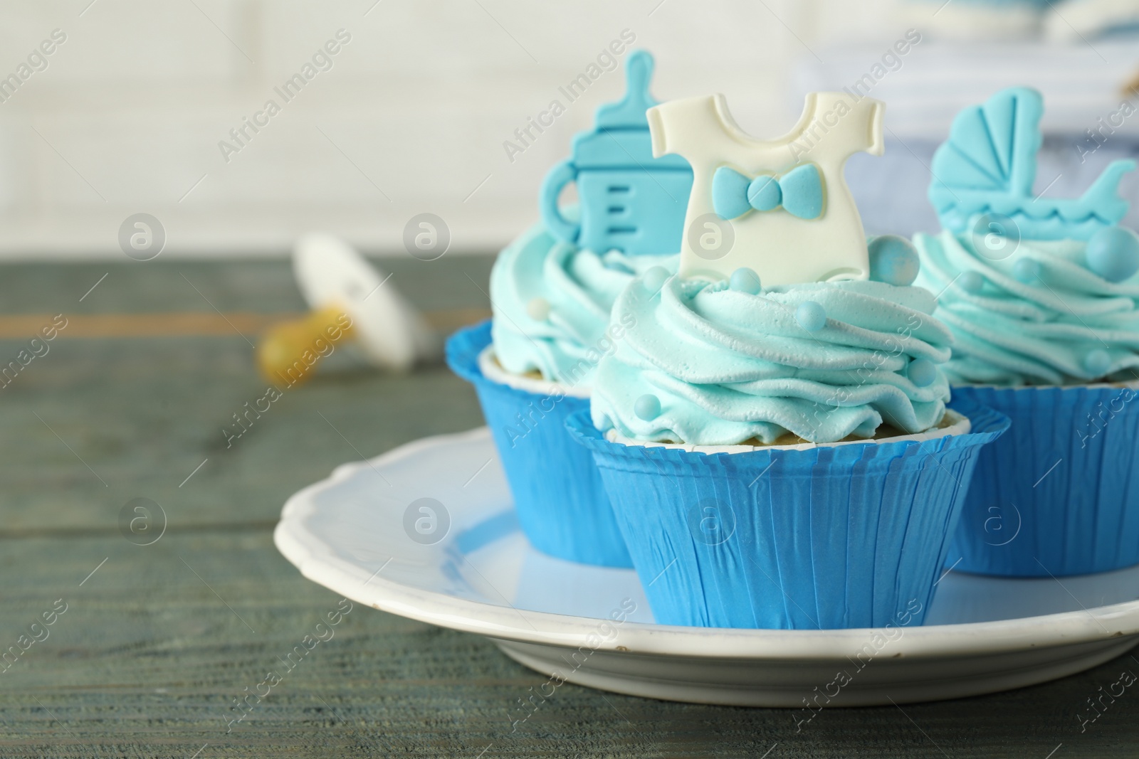 Photo of Beautifully decorated baby shower cupcakes with cream and boy toppers on grey wooden table. Space for text