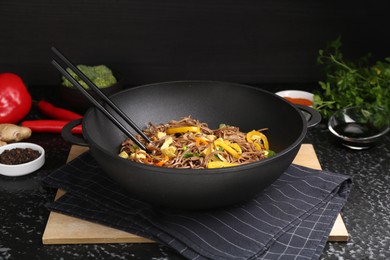 Stir-fry. Tasty noodles with vegetables, meat and chopsticks in wok on dark textured table