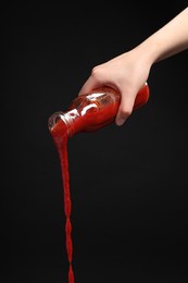 Photo of Woman pouring tasty ketchup from bottle on black background, closeup