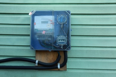 Photo of Electric meter on turquoise wooden wall outdoors, space for text. Measuring device
