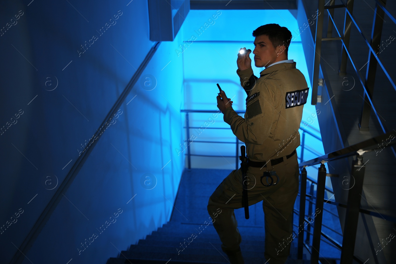 Photo of Professional security guard with flashlight and portable radio set on stairs in dark room