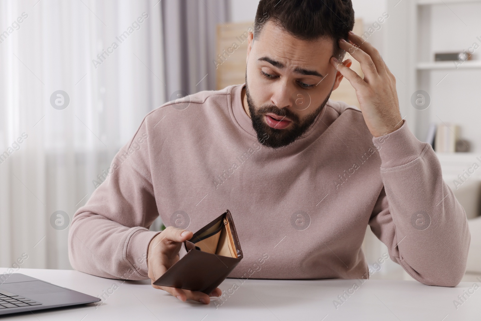 Photo of Confused man with empty wallet at white table indoors