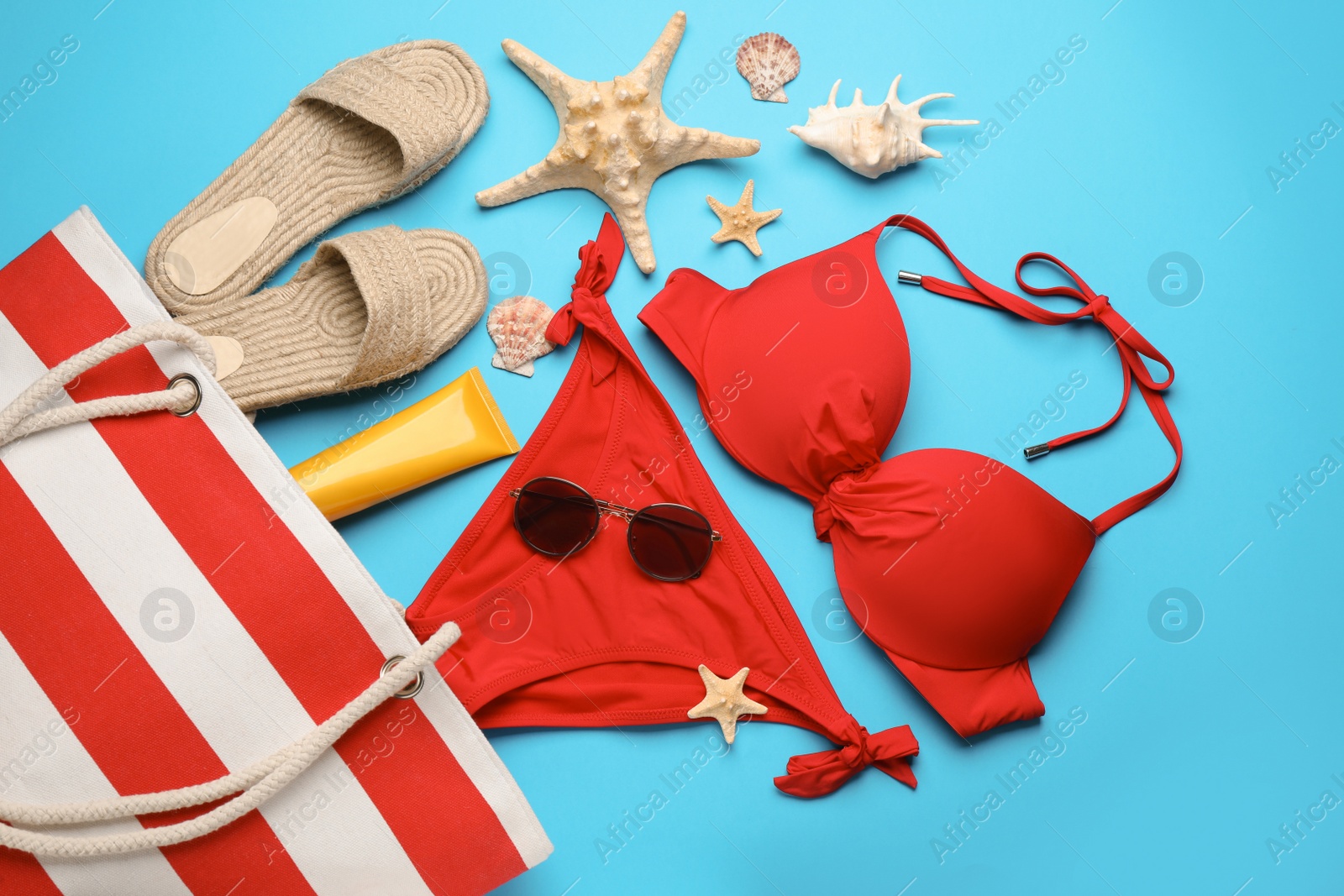 Photo of Stylish bag with beach accessories on light blue background, flat lay