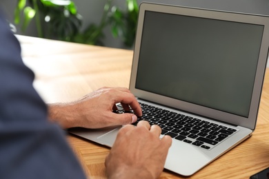 Photo of Man using laptop for search at wooden table indoors, closeup