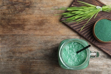 Photo of Flat lay composition with spirulina smoothie, powder and wheat grass on wooden background. Space for text