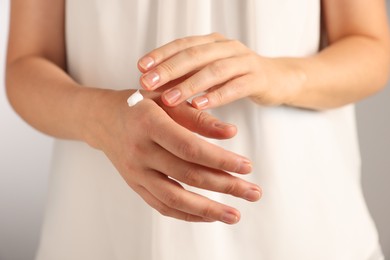 Photo of Woman applying cosmetic cream onto hand against light grey background, closeup