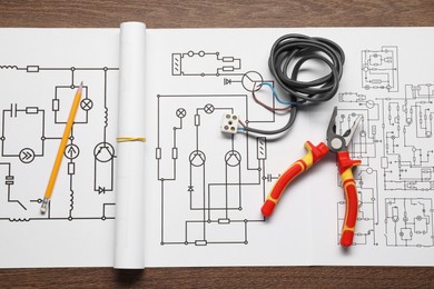 Photo of Wiring diagram, pencil, wires and pliers on wooden table, top view