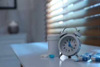 Photo of Alarm clock and pills on white table indoors, space for text. Insomnia treatment
