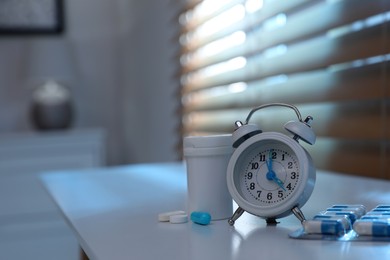 Alarm clock and pills on white table indoors, space for text. Insomnia treatment