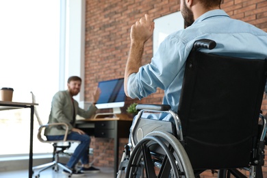 Young man in wheelchair with colleague at office, closeup