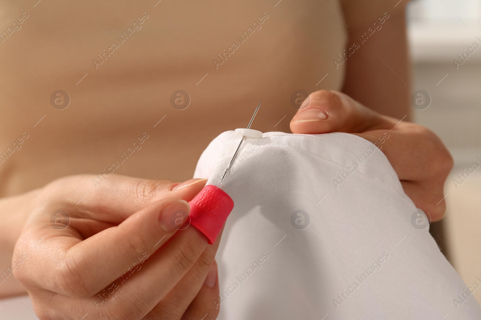 Photo of Woman sewing on white fabric with thimble and needle, closeup