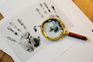 Magnifying glass and handprints on desk, flat lay. Detective's workplace