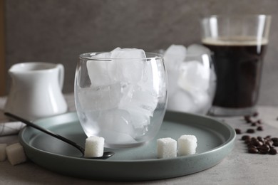 Photo of Making iced coffee. Ice cubes in glass, ingredients and spoon on gray table, closeup