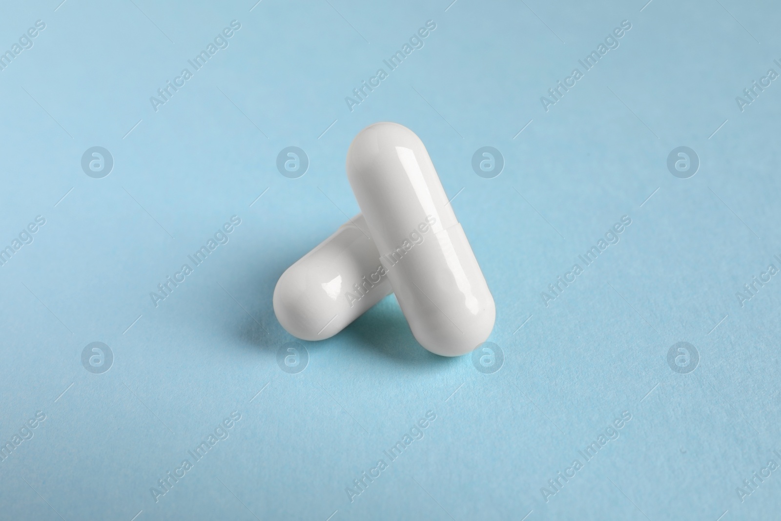 Photo of Two white pills on light blue background, closeup