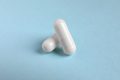 Two white pills on light blue background, closeup