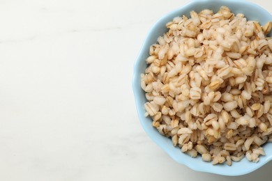 Photo of Delicious pearl barley in bowl on white marble table, top view. Space for text