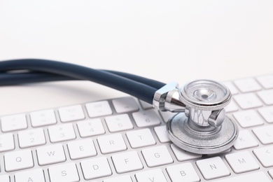 Photo of Modern keyboard and stethoscope on light background. Technical support concept