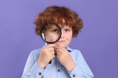 Photo of Cute little boy looking through magnifier glass on violet background